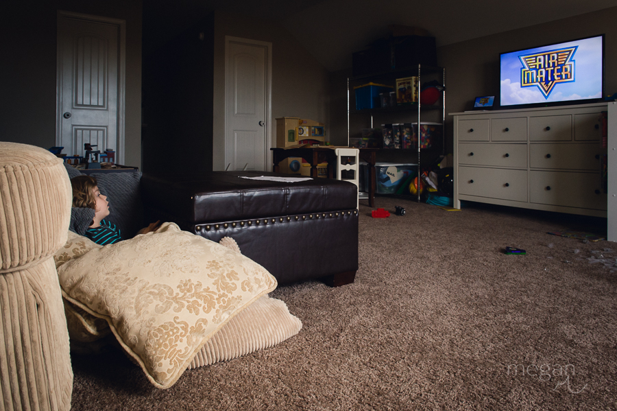 toddler sits amongst couch pillows on floor while watching tv